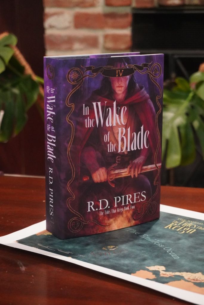 The standard hardcover edition of In the Wake of the Blade, book four in The Tides That Reign saga standing upright on a canvas map from the series. 