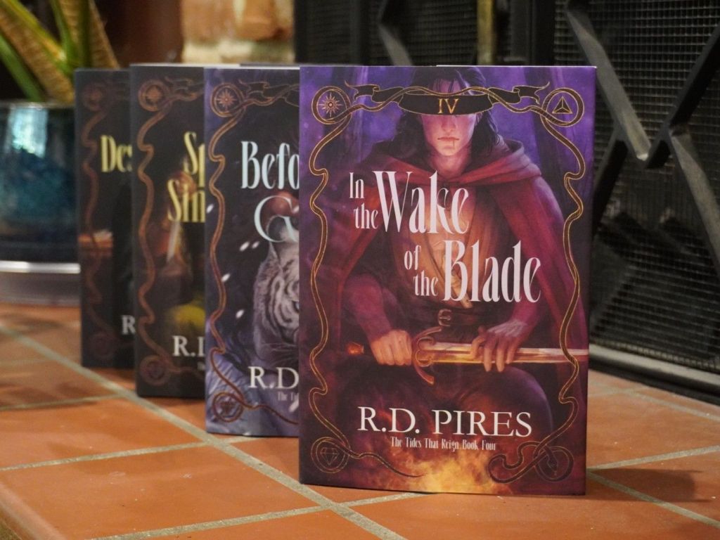 Hardcover editions of the four book in The Tides That Reign queer, dark epic fantasy series lined up on the tile hearth of a fireplace.