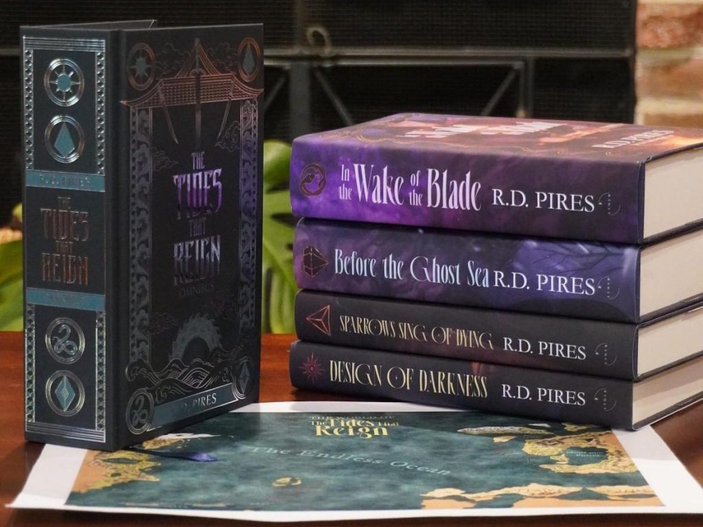 Five books atop a fantasy map on a table. One, The Tides That Reign omnibus, stands upright on the left, while the four individual entries in The Tides That Reign epic fantasy saga are stacked on the right.