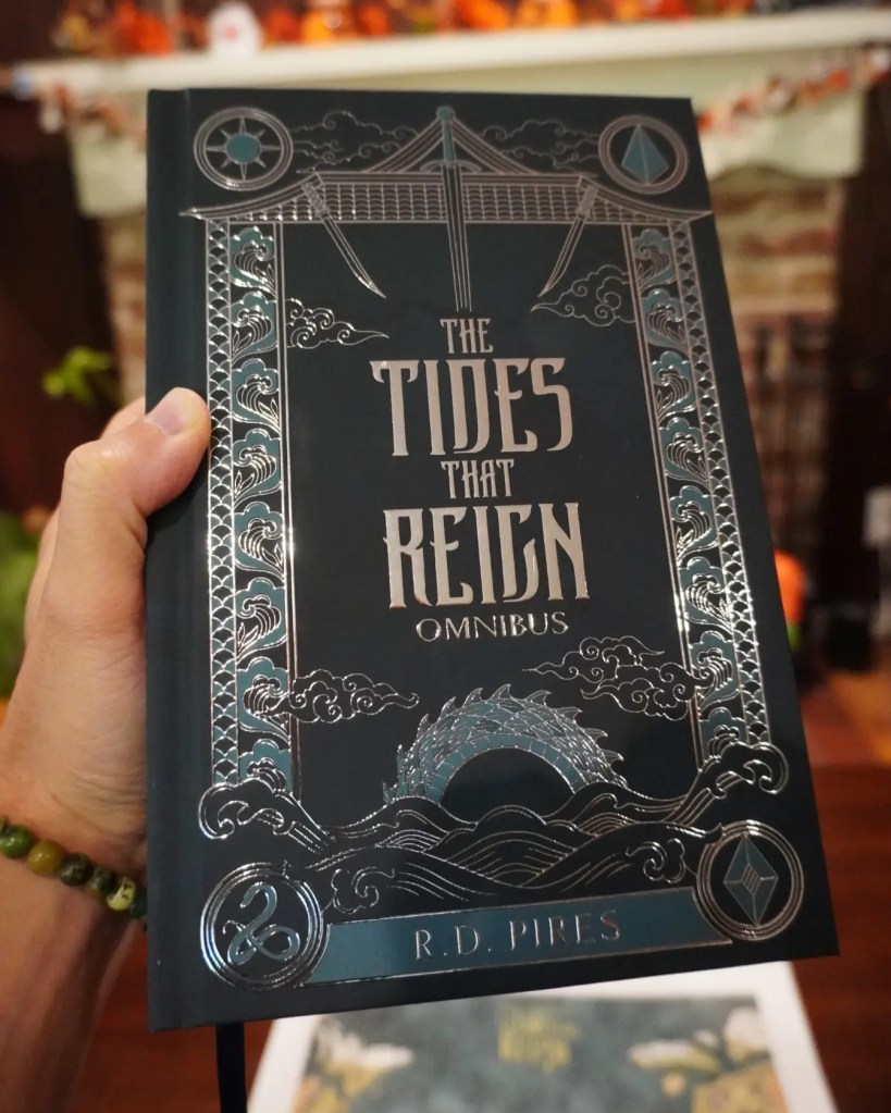 Holding a hardcover copy of The Tides That Reign epic fantasy saga series omnibus.